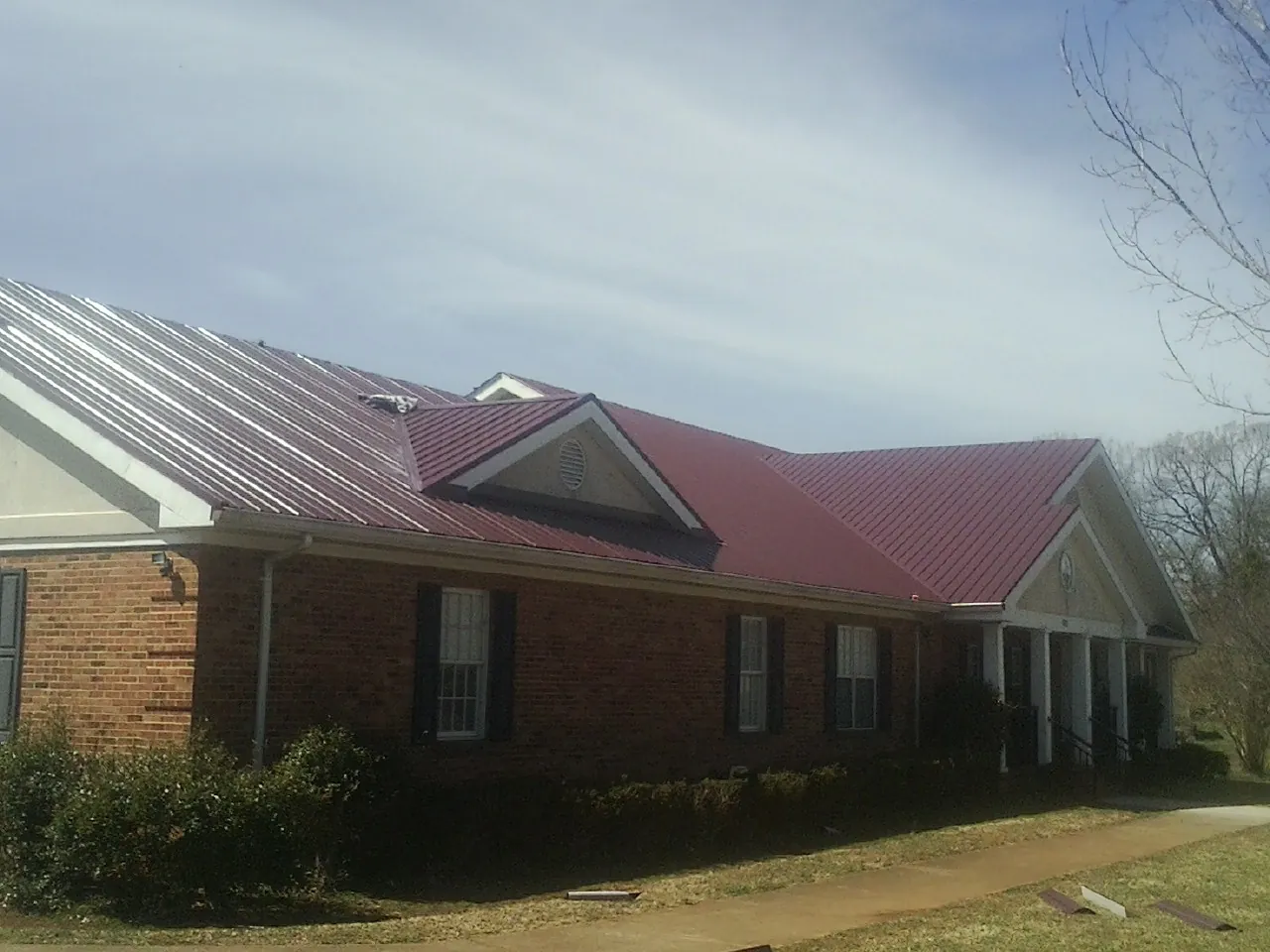 Red metal roof with gabled entries on a long brick building, from a Hail Damage Roof Repair job in Bluffton