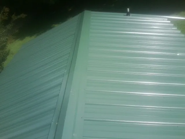 New green metal panels meeting at the ridge of a roof — Flat Roof Repair work by our crew in Bluffton